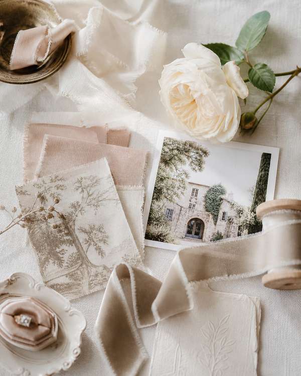 A wedding mood board with fabric swatches in blush and ivory, ribbon samples, and a cream garden rose