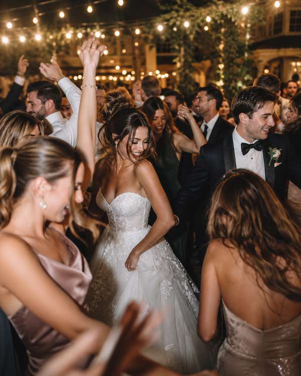 A packed wedding dance floor at night with guests dancing under warm string lights