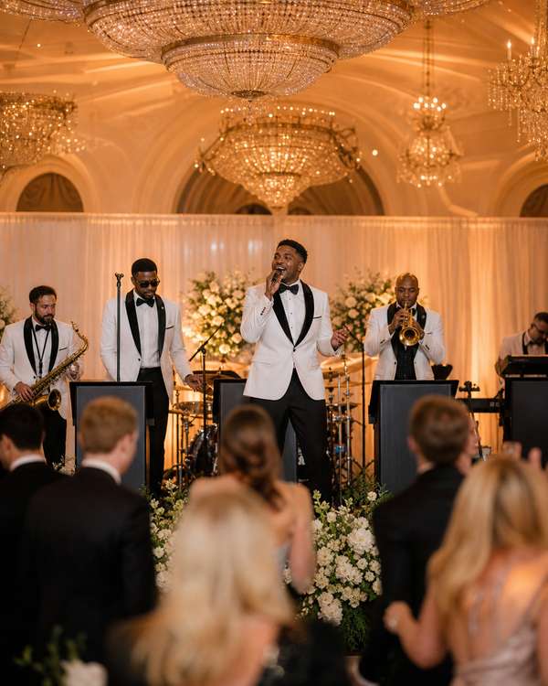 A sophisticated live wedding band on stage at an elegant indoor reception with chandeliers and warm uplighting