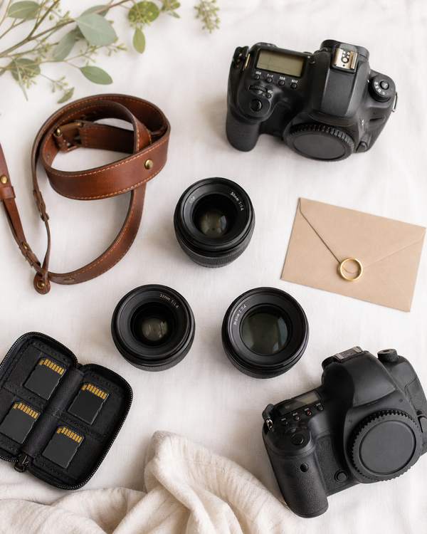 A flat-lay of professional wedding photography gear: DSLR bodies, prime lenses, and a leather strap