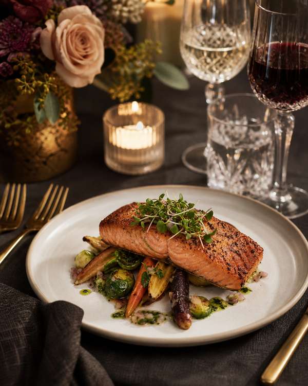 An elegantly plated wedding dinner of seared salmon with seasonal vegetables on charcoal linen with crystal and gold flatware